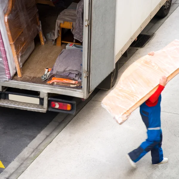 Un homme porte un meuble volumineux devant un camion de déménagement, illustrant les erreurs à éviter lors d'un déménagement.